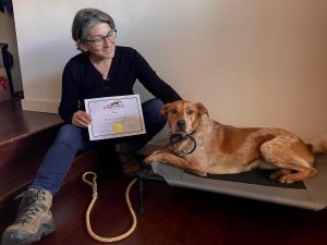 a dog and a woman sitting next to each other, holding up a graduation certificate.