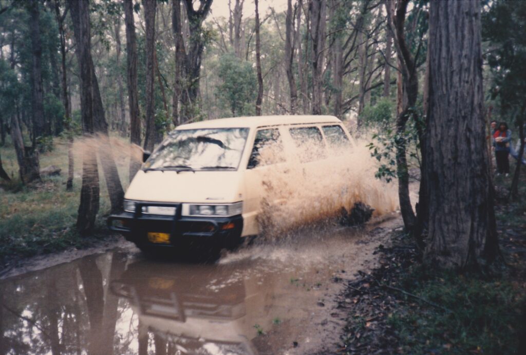Picture of a minivan splashing through a drowned road in a pine forest in New South Wales