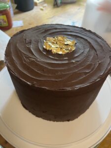 8 inch three tier chocolate cake with chocolate frosting, decorated with torn gold paper in the center of the top.